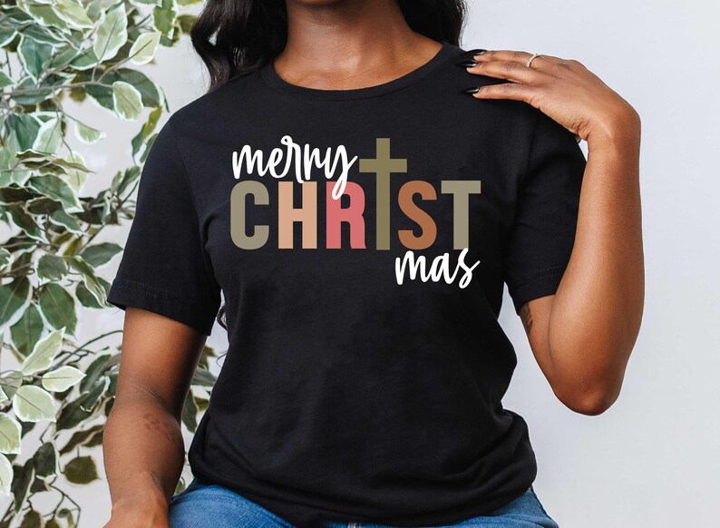 Pu&ograve; includere: Una maglietta nera con il testo "merry CHRISTmas" in lettere colorate. La parola "CHRIST" &egrave; in un carattere pi&ugrave; grande rispetto alle altre parole. Una croce &egrave; centrata sopra la parola "CHRIST".