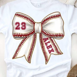 May include: White t-shirt with a red and white baseball bow. The bow has the number 23 and the name Alex on it.