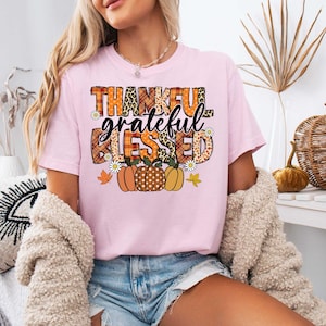 K&ouml;nnte beinhalten: Rosa T-Shirt mit einem grafischen Design, das "Thankful Grateful Blessed" mit herbstlichen K&uuml;rbissen und Bl&auml;ttern sagt.