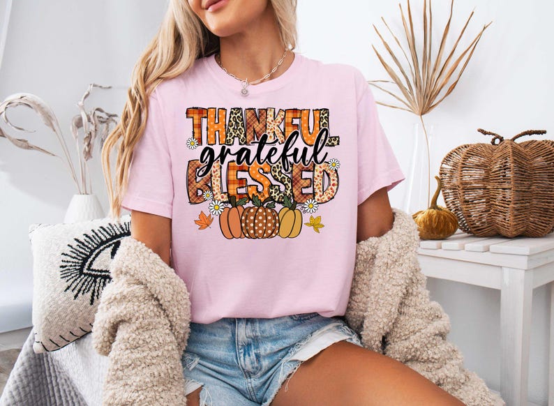 K&ouml;nnte beinhalten: Rosa T-Shirt mit einem grafischen Design, das "Thankful Grateful Blessed" mit herbstlichen K&uuml;rbissen und Bl&auml;ttern sagt.