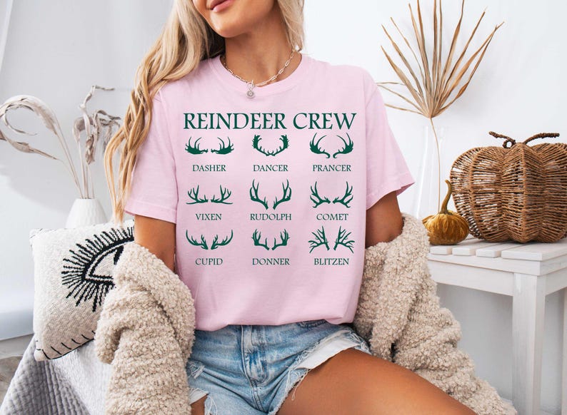 Pu&ograve; includere: Maglietta rosa con il testo "Reindeer Crew" e una grafica di corna di renna con i nomi di ogni renna: Dasher, Dancer, Prancer, Vixen, Rudolph, Comet, Cupid, Donner, Blitzen.
