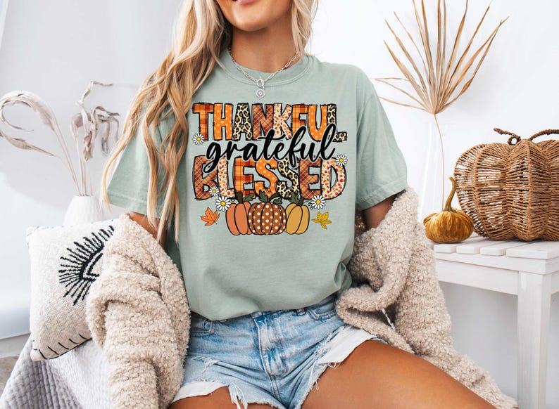 K&ouml;nnte beinhalten: Ein hellgr&uuml;nes T-Shirt mit dem Text "thankful grateful blessed" in einem Patchwork-Design mit Herbstfarben und K&uuml;rbissen.