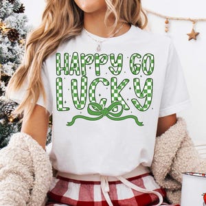 May include: White t-shirt with green and white checkered text that reads "Happy Go Lucky" with a green bow.