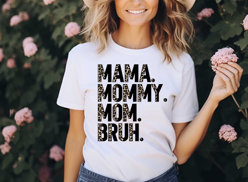 Puede incluir: Camiseta blanca con las palabras "MAMA. MOMMY. MOM. BRUH." impresas en negro y estampado de leopardo. La camiseta es de estilo casual, adecuada para el uso diario. El dise&ntilde;o es una versi&oacute;n divertida y moderna de la maternidad.