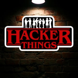 May include: A black and red sticker with the text "Hacker Things" in white letters. The sticker features a row of white silhouette figures in front of the text.