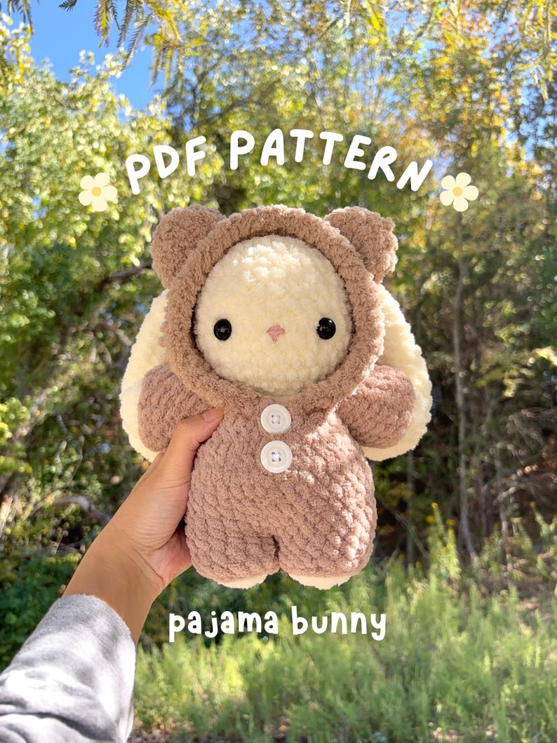 May include: A crocheted bunny toy in a brown pajama suit with a hood and white buttons. The bunny has cream-coloured fur and black eyes. The image includes the text "PDF PATTERN" and "pajama bunny".