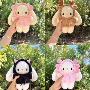 May include: Four handmade crochet bunny dolls, each with a unique hooded outfit. The outfits include a pink deer, brown deer, black cat, and pink flower design. The bunnies are white with black eyes and noses, and the outfits have matching details.