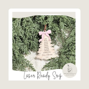 May include: A wooden Christmas tree decoration with a pink bow and a brown string. The ornament is engraved with names and the text "Mrs. O'Brien 2025". The ornament is surrounded by green foliage.