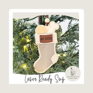 May include: A Christmas stocking ornament for dogs, featuring a tennis ball and bone. The stocking is beige with a textured pattern and a brown leather-like tag that reads "#1 DOG". The ornament hangs from a brown string and is set against a backdrop of green Christmas tree branches.