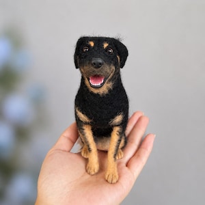 May include: A needle-felted dog figurine featuring black and tan fur, a black nose, and an open mouth showing white teeth. The small, textured sculpture is crafted with a realistic appearance, capturing the alert expression of a canine.