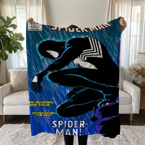 May include: A blue Spider-Man blanket featuring a comic book cover design. The blanket showcases Spider-Man in a black suit with white web detailing, set against a blue background with rain effects. Text includes "Spider-Man" and "Introducing the New".