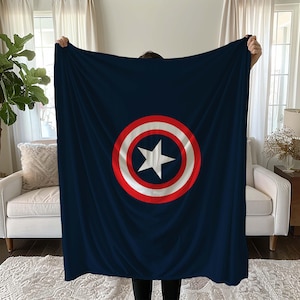 K&ouml;nnte beinhalten: Eine marineblaue Fleece-Decke mit einem roten und wei&szlig;en Captain-America-Schild-Design.