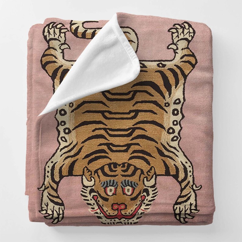 May include: A pink and brown tiger rug with a white fleece blanket folded on top. The tiger is depicted with a detailed pattern of stripes and a fierce expression.