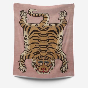 May include: A pink tapestry featuring a brown and black tiger rug design. The tiger is lying on its back with its paws in the air. The tiger has a black nose, white teeth, and blue eyes.