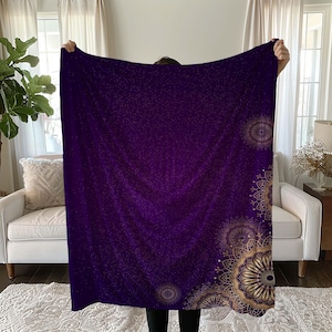 May include: A purple fleece throw blanket with a gold mandala pattern on the bottom right corner. The blanket has a subtle sparkle effect.