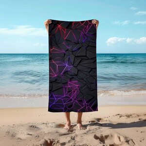 Könnte beinhalten: Ein schwarzes Strandtuch mit einem geometrischen Muster aus rosa und violetten Linien. Das Handtuch ist aus einem weichen, saugfähigen Material gefertigt und perfekt zum Abtrocknen nach dem Schwimmen.