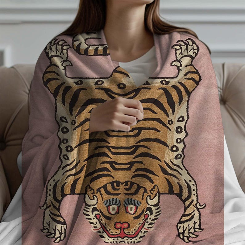 May include: A pink throw blanket featuring a tiger design. The tiger is depicted in a traditional style with orange and black stripes and a detailed face.