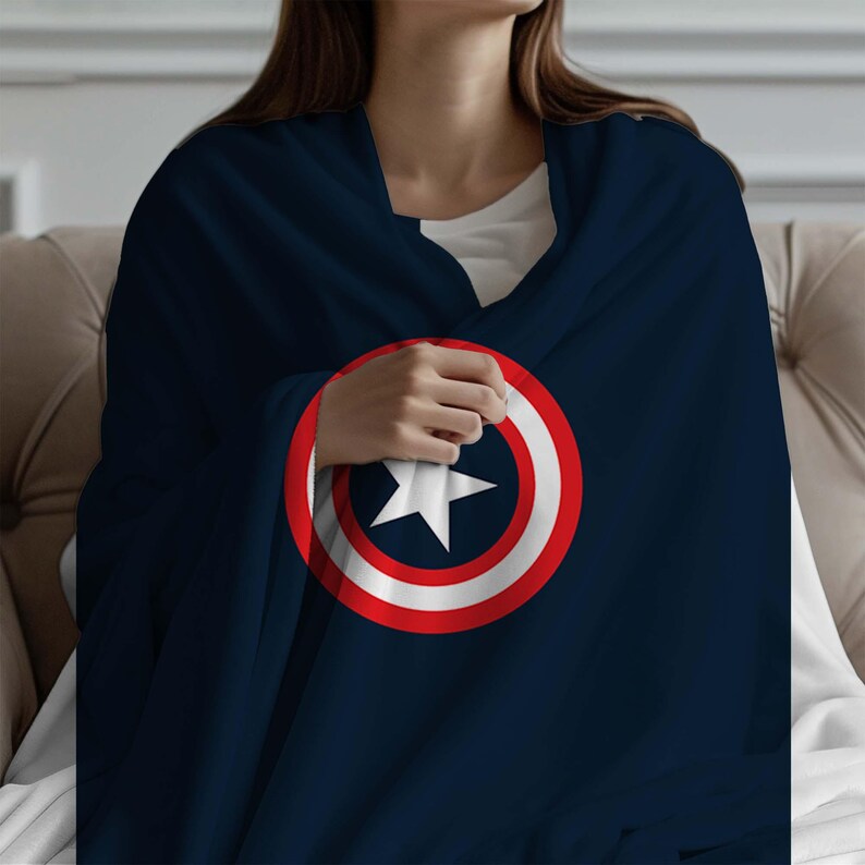 K&ouml;nnte beinhalten: Eine marineblaue Fleece-Decke mit einem roten, wei&szlig;en und blauen Captain-America-Schild-Design.