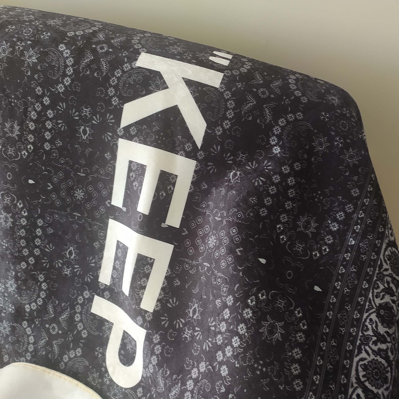 K&ouml;nnte beinhalten: Schwarz-wei&szlig;es Stoff mit Paisley-Muster. Das Wort "KEEP" ist in Wei&szlig; auf dem Stoff gedruckt.
