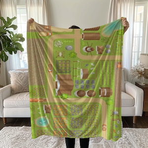 May include: A green and brown fleece blanket with a cartoon illustration of a farm scene. The blanket features a winding road, farmhouses, fields, and a windmill.