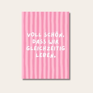 Könnte beinhalten: Eine rosa Karte mit vertikalen Streifen in verschiedenen Rosatönen. Die Karte zeigt den deutschen Text "VOLL SCHÖN, DASS WIR GLEICHZEITIG LEBEN." in weißer, handschriftlicher Schrift. Die Karte ist vor einem neutralen Hintergrund platziert.