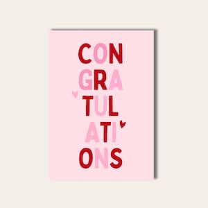 Könnte beinhalten: Eine rosa Glückwunschkarte mit dem Wort "CONGRATULATIONS" in vertikaler Anordnung. Die Buchstaben sind in Rot- und Rosatönen gehalten, mit kleinen Herzakzenten. Der Hintergrund ist einfarbig hellrosa.