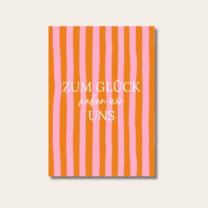 Può includere: Una carta rettangolare con un motivo a righe verticali arancioni e rosa. Il testo "ZUM GLÜCK haben wir UNS" è scritto in bianco, con la parola "haben" in corsivo. La carta è su uno sfondo color crema.
