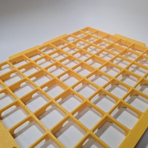 May include: A yellow plastic grid with a square pattern. The grid is made of interconnected squares, creating a lattice-like structure. The object is likely used for organization or support.