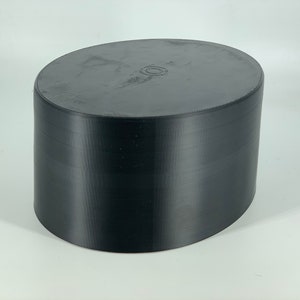 May include: A black, oval-shaped, 3D printed object with a smooth, textured surface.