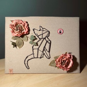 May include: A black wire cat sculpture on a beige canvas background with two pink fabric flowers. The canvas has a small brown label that says "hand made with love". There is a pink circle sticker with a black paw print and the text "Stay Awesome".