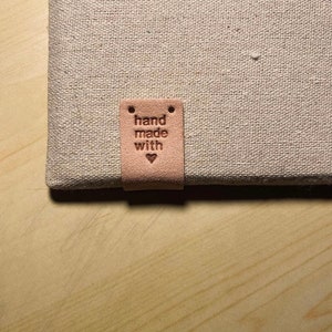 May include: A light brown leather tag with the text "hand made with" and a small heart symbol.