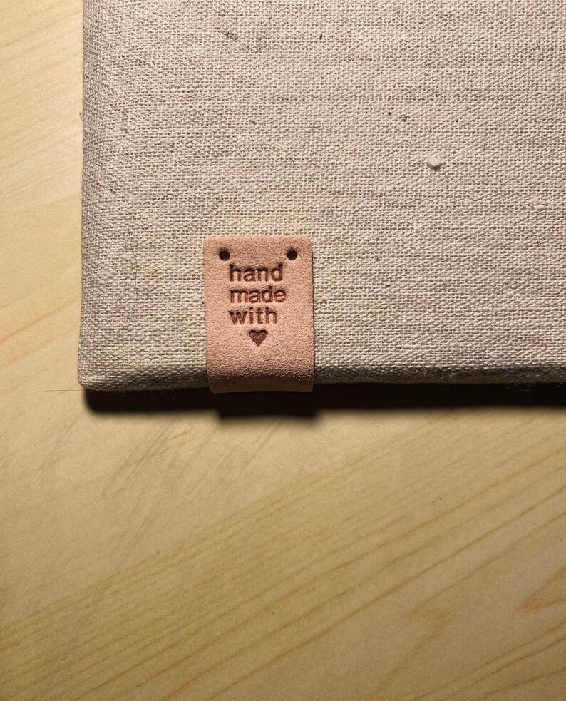 May include: A light brown leather tag with the text "hand made with" and a small heart symbol.