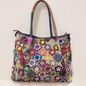 Könnte beinhalten: Eine mehrfarbige Ledertasche mit Patchwork-Design und Blumenausschnitten. Die Tasche hat zwei Henkel oben und einen Reißverschluss.