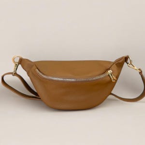 Peut inclure: Une banane en cuir marron avec une fermeture éclair dorée et une sangle réglable.