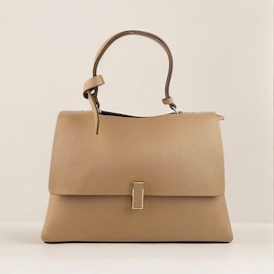 Peut inclure: Un sac à main en cuir beige avec une poignée supérieure et un fermoir doré. Le sac a une forme structurée et une finition texturée.