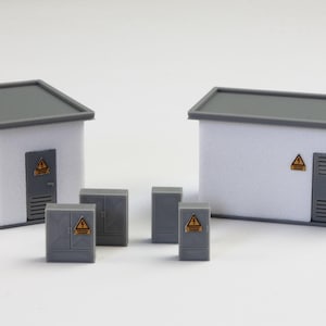 Pode incluir: Miniaturas de edifícios brancos com telhados e portas cinzentas, juntamente com caixas elétricas cinzentas menores. Cada estrutura apresenta um símbolo de aviso amarelo e preto, sugerindo um modelo de subestação elétrica.