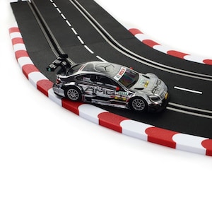Peut inclure: Une voiture de course jouet argentée avec des accents rouges et blancs sur une piste de course noire avec des bordures rouges et blanches.