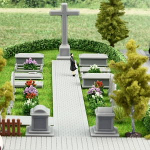 Può includere: Un modello di cimitero in miniatura con una croce grigia centrale, diverse lapidi grigie, paesaggio verde, piccoli gruppi di fiori colorati, una singola figura in piedi e un piccolo veicolo argentato parcheggiato su un sentiero lastricato.