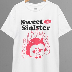 Puede incluir: Camiseta blanca con un gráfico rojo y negro de un diablo de dibujos animados con llamas y el texto "Sweet but Sinister".