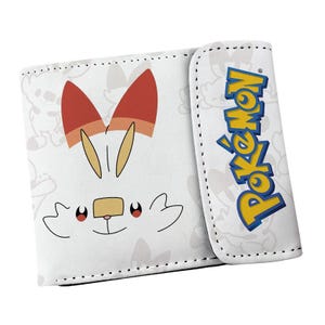 May include: A white bi-fold wallet featuring a graphic of the Pokemon character Scorbunny on the front. The wallet has a flap closure with the blue and yellow Pokemon logo printed vertically on the right side and a subtle grey pattern.