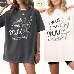 May include: Two oversized t-shirts with a graphic design of a woman in a champagne glass with the text "girls gone mild" and "Emily's Bachelorette Miami, Florida 2025". The shirts are shown in two colors: pepper and ivory.