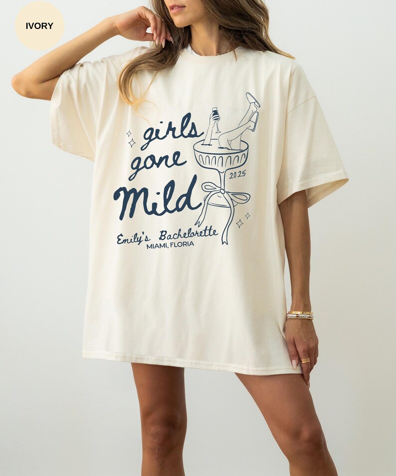 May include: Ivory oversized t-shirt with a graphic of a woman in a champagne glass. The text on the shirt reads "girls gone mild" and "Emily's Bachelorette Miami, Florida".
