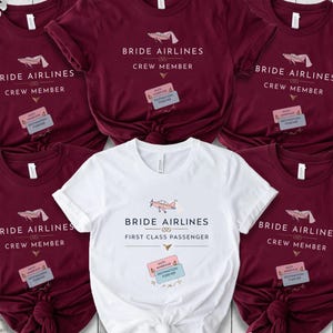 Puede incluir: Cinco camisetas marrones con el texto "Bride Airlines Crew Member" y un pequeño gráfico de avión. Una camiseta blanca con el texto "Bride Airlines First Class Passenger" y un pequeño gráfico de avión. Todas las camisetas tienen un pequeño gráfico de tarjeta de embarque con el texto "Gate Marriage Destination Forever".