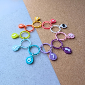 May include: A collection of colorful number charms, each with a ring and a number from one to eight. The charms are in various colors, including orange, yellow, pink, white, purple, and blue. The background is a mix of blue and brown.