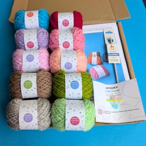 May include: A craft kit containing balls of yarn in shades of blue, pink, green, and brown. The kit includes knitting needles and instructions. The packaging features the text "ARTHUR'S Craft Corner".