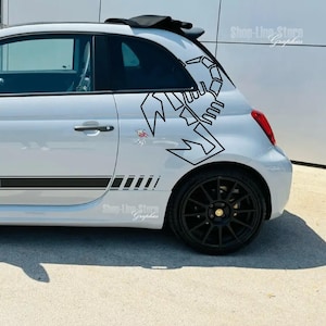 Pode incluir: Um Fiat 500 prateado com um adesivo de escorpião preto na porta traseira. O carro tem listras de corrida pretas na lateral e rodas pretas.