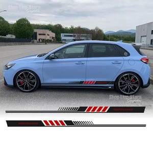 Op de afbeelding: Een lichtblauwe auto met zwarte en rode race strepen langs de zijkant. De strepen hebben het woord "PERFORMANCE" erop gedrukt.