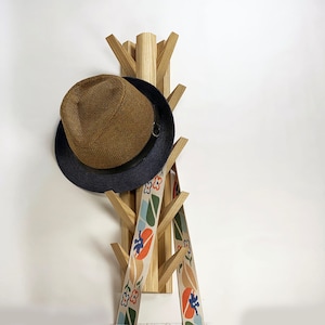 May include: A wooden coat rack with a hat and two patterned straps hanging from it. The rack is shaped like a tree with multiple branches.