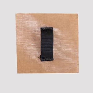 May include: A square piece of brown fabric with a black fabric handle.