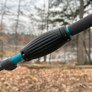 May include: Close-up of a black trekking pole with a blue adjustable section and a textured black grip.